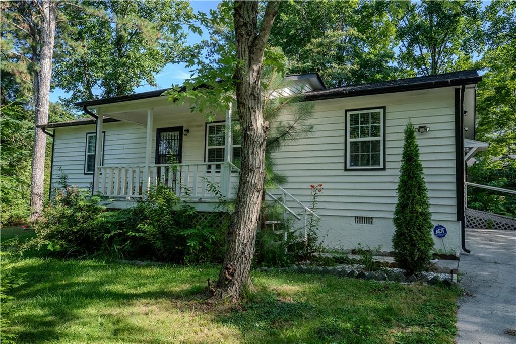 Single-story residence featuring white siding, a covered front porch with white railing, a black security screen door, and a partially paved driveway