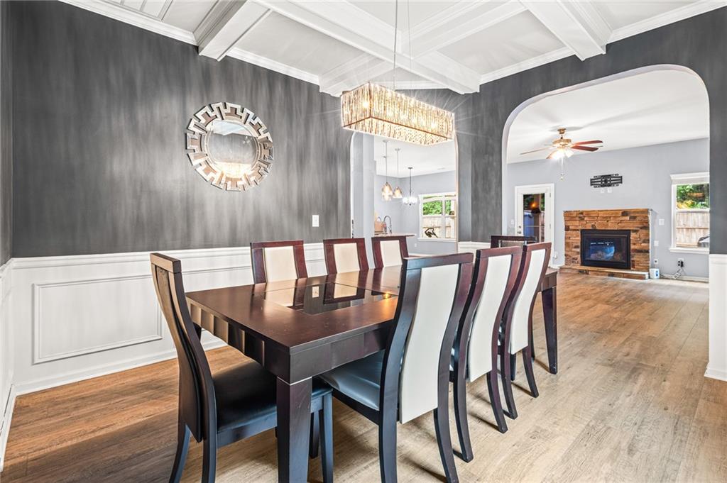 Coffered ceiling dining area featuring wood-finish flooring, wainscoting, and an arched entry