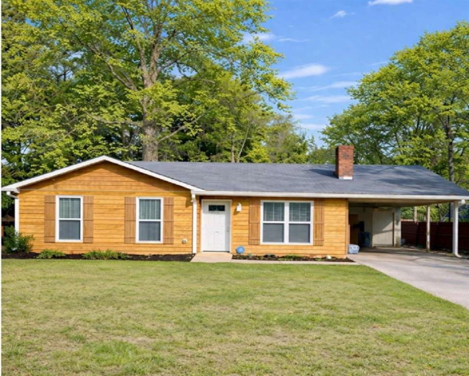 Single story home with an attached carport, a chimney, a front yard, and driveway