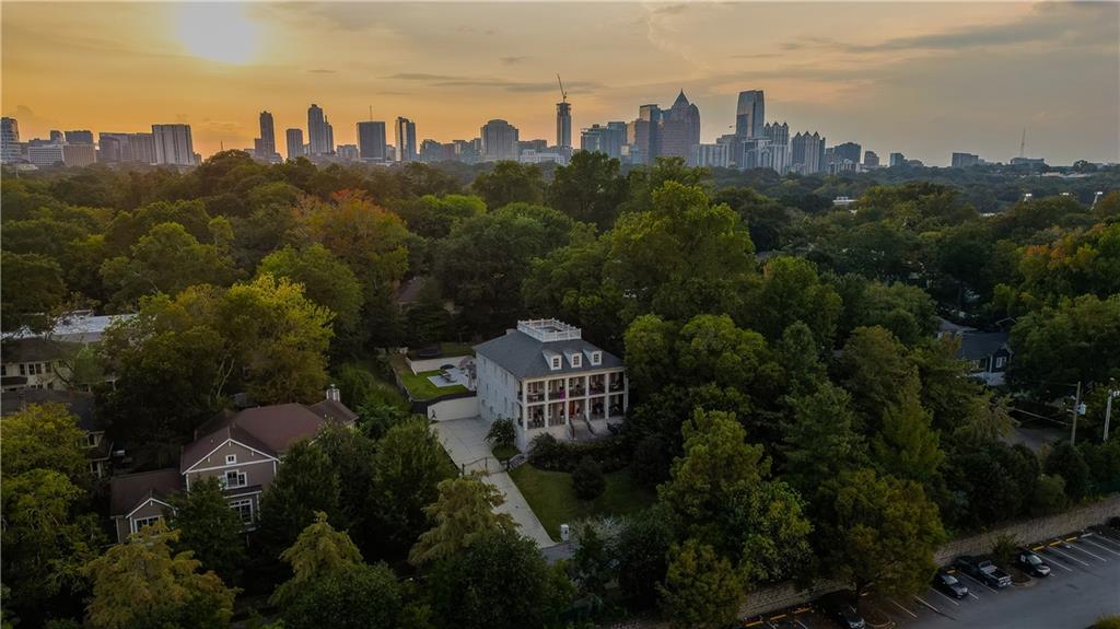 Welcome to an icon of Midtown—where modern-antebellum elegance and resort-style amenities meet on the largest residential lot in the Garden District. Tucked quietly away from the street, yet instantly recognizable from the BeltLine, this residence commands attention with its double-height verandas, elevated site, and a one-of-a-kind widow’s walk offering sweeping 360° skyline views and sunsets you won’t forget.
Completed in 2017 and thoughtfully expanded since, the home unfolds across 6,898 finished square feet on four levels, delivering eight bedrooms and seven and a half baths. The classic facade is lined with eight sets of French doors, flooding the main floor with light and opening directly onto the verandas. Ten-foot ceilings crown the main level, which also boasts its own laundry for added convenience.
Step outside to a heated salt-water pool, perfectly positioned for privacy and effortless entertaining, with two additional sets of French doors leading to the backyard oasis.
The vaulted owner’s retreat is a world unto itself—enjoy serene pool views, direct access to the veranda, a separate sitting room with a mini wet bar, and a private connection to an adjoining bedroom ideal for a nursery or home office.
On the third floor, another laundry room—complete with a sink and generous folding space—makes everyday living seamless. The fourth level offers two spacious bedrooms, abundant attic storage, a Jack-and-Jill bath, and access to the rooftop deck, where the city unfolds in every direction.
Downstairs, host guests in a private suite, stay active in the professional gym, unwind in the steam shower, and rest easy with a concrete-encased panic room. The three-car garage is EV-ready for modern convenience.
Estate-scale grounds blend with Midtown’s walkability: stroll three minutes to the Eastside BeltLine Trail, Home Depot, Whole Foods, Trader Joe’s, and Ponce City Market; Piedmont Park is just a ten-minute walk away.
This is more than a home—it’s Midtown’s landmark estate, offering rare land, unforgettable views, and the kind of privacy and access that’s only possible here.