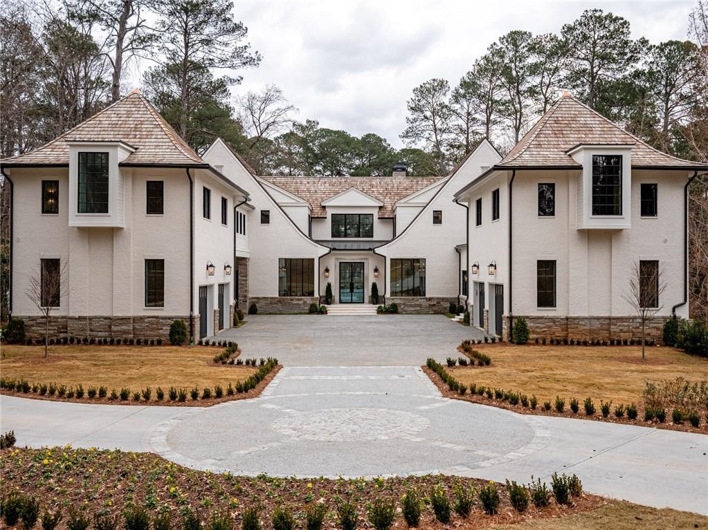 Tucked away on one of the most sought-after streets in the heart of Buckhead, an exquisite collaboration between Harrison Design and White Oak Fine Homes produced this inspired transitional style home completed in Dec. 2021. From the impressive steel front entry doors to the extensive use of natural stone elements, Venetian plaster and other bespoke touches, it’s apparent that no detail was overlooked in crafting this one-of-a-kind tour de force of design executed by the O’Donnell Group. An open and inviting layout features soaring arched ceilings and a large expanse of windows positioned to bathe the space with natural light and provide breathtaking views of the pool and manicured grounds. Envisioned to accommodate everything from the flow of daily life to entertaining on a grand scale, the show-stopping kitchen is anchored by a dramatic 11’ waterfall edge island enrobed with Calacatta marble extending to the countertops and backsplash behind the Wolf range and custom designed range hood.  From the kitchen, the floorplan opens to a sunny breakfast room and dramatic living room anchored by a massive 48” fireplace with custom limestone mantle and hearth.  The main level primary bedroom suite features a dramatic vaulted ceiling, arched windows, large natural stone fireplace and private access to the pool and gardens. Custom designed dual closets and an elaborate bath with heated Blavet Blanc limestone floors, floor-to-ceiling Amalfi satin tile, a glass surround walk-in shower with dual shower heads, separate oversized soaking tub and custom cabinetry complete this opulent owner’s retreat. Additional enviable features include a spectacular wet bar and wine cellar cabinet with space for 300 bottles, a virtual learning room, finished daylight terrace level, and an additional upper-level guest suite with private entrance.