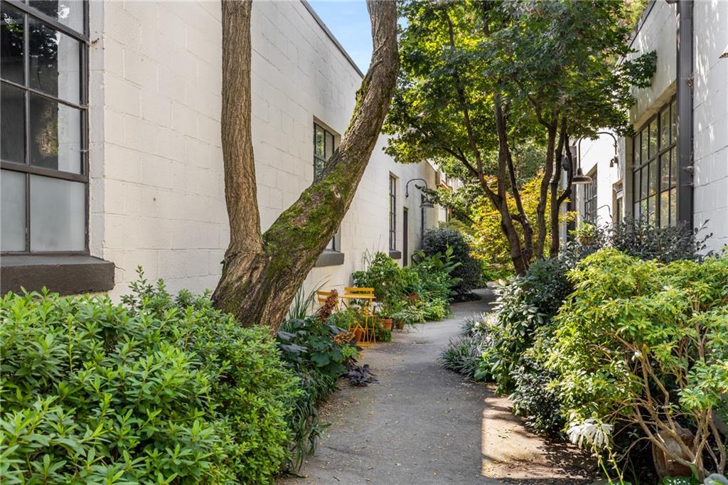 This is the kind of loft that makes you want to stay awhile. Once the original storefront of a historic motor factory, this two-bedroom, two-bath home carries a sense of history that you can feel the moment you walk in. The dramatic steel window on the main level is pure magic, capturing the light, the trees outside, and the energy of the neighborhood beyond.
Inside, polished concrete floors flow into warm pine upstairs, setting the stage for spaces that are as comfortable as they are striking. The floating staircase feels like a piece of art, connecting two living levels that invite creativity, think home office, media lounge, yoga space, or just a perfect spot to curl up with a book. Updated kitchen and baths mean you get character without sacrificing modern convenience.
And then there’s what’s outside your door. The community feels like a hidden garden in the middle of the city, with lushly planted paths, mature trees, and the sound of water from the central fountain, an everyday escape from the bustle. Two deeded parking spaces make coming and going easy, but you may not need your car much with everything right here.
Want your morning coffee? Just steps away. Ready to hop on the Beltline for an evening ride? It’s two blocks over. Craving dinner with friends? Some of Atlanta’s best restaurants are right around the corner. Want to see a play? There are three theaters practically outside your door. In the mood for live music or a concert? The neighborhood’s venues have you covered.
This is more than just a place to live; it’s a chance to be part of a neighborhood with parks, transit, dining, shopping, and entertainment all outside your gated complex. If you’ve been waiting for a home with story, soul, and a lifestyle that puts you at the center of it all, this is the one.