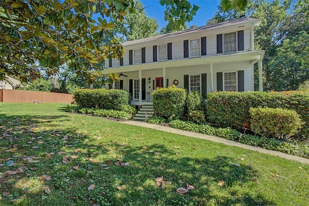 Two-story colonial-style home featuring a covered front porch, white siding, dark shutters, and a red front door