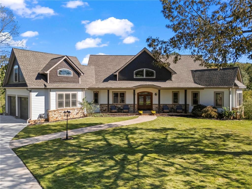 There are homes that impress, and then there are homes that speak. This one doesn’t raise its voice. It doesn’t have to. It welcomes you with quiet confidence, the kind that only comes from craftsmanship, intention, and soul. Tucked within a peaceful enclave of custom-built homes, this refined estate rests gracefully on nearly four private acres with a fully stocked lake glistening just beyond the back porch. The sound of nature replaces the noise of traffic. The air feels lighter here, as if life slows down the moment you turn into the drive. The rocking-chair front porch nods to timeless Southern charm and opens to an interior defined by warmth, light, and texture. Cathedral ceilings soar above massive wood beams while floor-to-ceiling windows capture serene views of the lake and landscape. A stacked-stone fireplace anchors the living room, flanked by built-in bookcases that whisper stories of cozy evenings and connection. This is where elegance meets ease, where you can host a holiday gathering one night and sip coffee by the fire the next morning in peace. The heart of the home is the chef’s kitchen, designed for those who love to cook and connect with others. A 5x7 island doubles as prep space and conversation hub, while premium Wolf appliances deliver professional performance. Travertine flooring, undercabinet lighting, soft-close drawers, and thoughtful storage add both function and beauty. Two outdoor living areas extend the experience, one a grill porch for alfresco dining, the other a sweeping back porch with panoramic lake views. The main-level primary suite is a sanctuary of light and calm with hardwood floors, custom trim, and direct porch access for quiet mornings and sunsets. The spa-like bath features a jetted soaking tub framed by lake views, dual vanities, and a walk-in shower that feels like a retreat. Remote-controlled blinds add comfort and privacy, while the custom closet offers refined organization. Also on the main floor: a guest bath, laundry/mudroom, and a dedicated office with beveled French doors, a built in and inspiring views. Upstairs, three spacious bedrooms and two full baths provide a thoughtful separation of space, perfect for family or guests. The fifth bedroom offers incredible flexibility, ideal for a teen suite, hobby studio, or media room. The finished terrace level continues the home’s craftsmanship with a wet bar, stacked-stone fireplace, entertainment areas, safe room, bedroom, and full bath. Bright by day and inviting by night, it opens to a flagstone patio and firepit overlooking the water, perfect for evenings under the stars. Step outside, and it feels like stepping into a storybook. The private lake, stocked with bass, grass carp, and bluegill, glimmers like glass. The owners have enhanced every inch of the property, clearing trees for views, rerouting drainage, extending the driveway, adding topsoil, and laying 35 pallets of Zoysia sod. Stamped concrete walkways, flagstone paths, irrigation, and fencing complete the landscape. A storage room beneath the porch doubles as a workshop or lawn maintenance garage. Every upgrade blends beauty with practicality: gutter guards, blown insulation, granite counters, lead-coated windows, and a whole-house speaker system. With its stunning lake backdrop, open lawns, and timeless lodge aesthetic, the property also serves as an ideal setting for parties and large get-togethers. Just 10 minutes from downtown Ball Ground and 15 minutes from shopping and dining, the location offers the best of both worlds, modern convenience wrapped in country calm. Add in Cherokee County’s low taxes, strong schools, and reputation for peace and privacy, and you’ll understand why this area is one of North Georgia’s most sought-after luxury enclaves. A home where craftsmanship, comfort, and connection come together, and where every detail feels like it was designed to be exactly, beautifully, here.