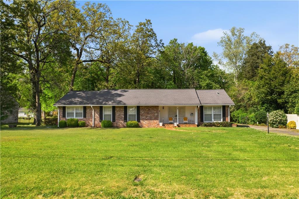 Brick ranch-style residence featuring a covered front porch, dark shutters, and a grey shingle roof