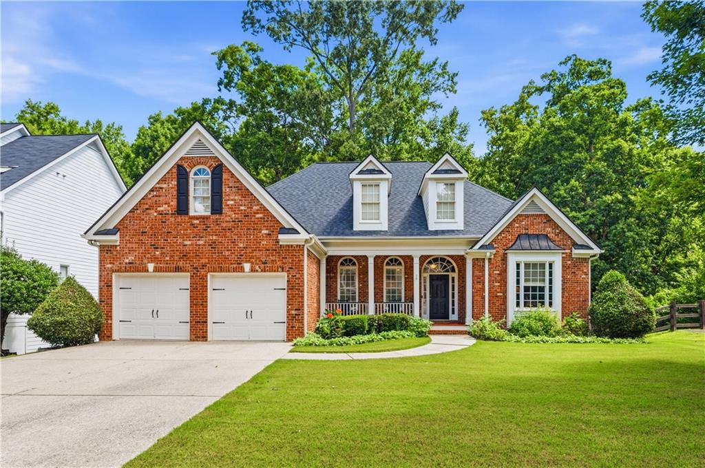 Brick facade residence featuring a two-car garage, covered entry porch with columns, a bay window, and gabled dormers