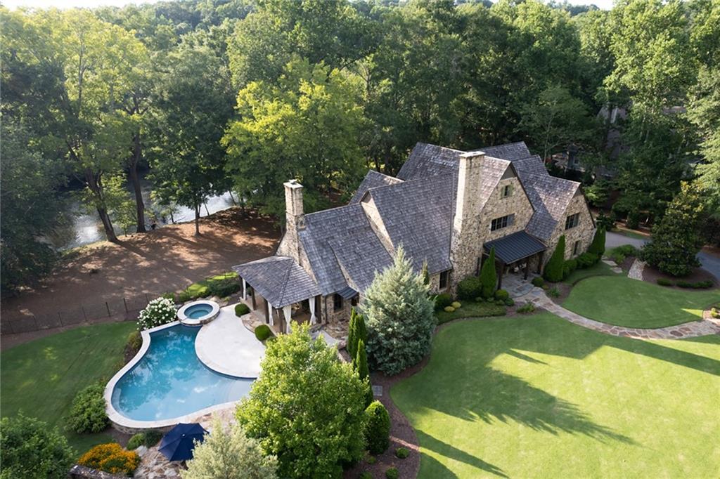 Set on a dreamy, wide-open tract of land that was once part of a small vineyard, this exquisite home offers endless views of the Chattahoochee River. Building 1714 Brandon Hall Drive, so close to the Chattahoochee River, was the culmination of four decades of home-building experience. Building Executive Terry Russell and his wife, Terrie, commissioned architect Greg Busch to design an architectural gem that showcased the magnificent Chattahoochee River in every room. Hand-split cedar shingles decorate the hand-chiseled old-world stone exterior, fashioned to resemble an English manor, while the interior offers clean lines, light-filled living spaces, soaring ceilings, spacious rooms and a harmonious floor plan with modern floor-to-ceiling structural wrought-iron steel windows/doors that open the entire home to the river. Loving attention to every detail and rare craftsmanship is in the bones of this home and echoes throughout all the finishes. Cedar rafter tails are sanded and shaped so they fit perfectly as tongue and groove, and the stone exterior is patterned to look like brick as it lengthens up the chimney. Designed to be a multi-generational gathering place to enjoy life on the river, this home allows you to savor the convenience of having everything you could possibly want at your fingertips: an oversized chef's kitchen with captivating river views, a 900-square-foot wine loft with retractable steel doors so the outside opens to the inside, a gunite Pebble Tec saline pool, a poolside outdoor kitchen and bathroom with a shower perfect for washing furry friends, a limestone fireside dining room, a 600+/- square foot yoga studio with soft cork floors, a sprawling front and side lawn, a waterfall jacuzzi with river views, six expansive porches that connect the modern interior to the breathtaking outdoors, a sleek wet bar that is perfectly accessible to the back porch, the best fly fishing on the Chattahoochee River, a beach-like riverfront perfect for launching kayaks and paddle boards, a tranquil place to sit and immerse yourself in the sound of the water and the sensation of the cool river breeze (always 10 degrees cooler by the river) and a perfect work-from-home retreat overlooking the calming river. Imagine waking up every morning to the fog rolling in and closing your eyes to the moonbeams on the glistening water. From the colors reflected on the water to the beautiful sunsets, the home was designed to revel in the endless connection to nature and the never-ending dance of the river. Set on one of the prettiest streets in Atlanta, with complete privacy because of two uninhabited islands and conveniently within 20+/- miles of everything Downtown Atlanta offers, this is a once-in-a-lifetime opportunity to have it all.