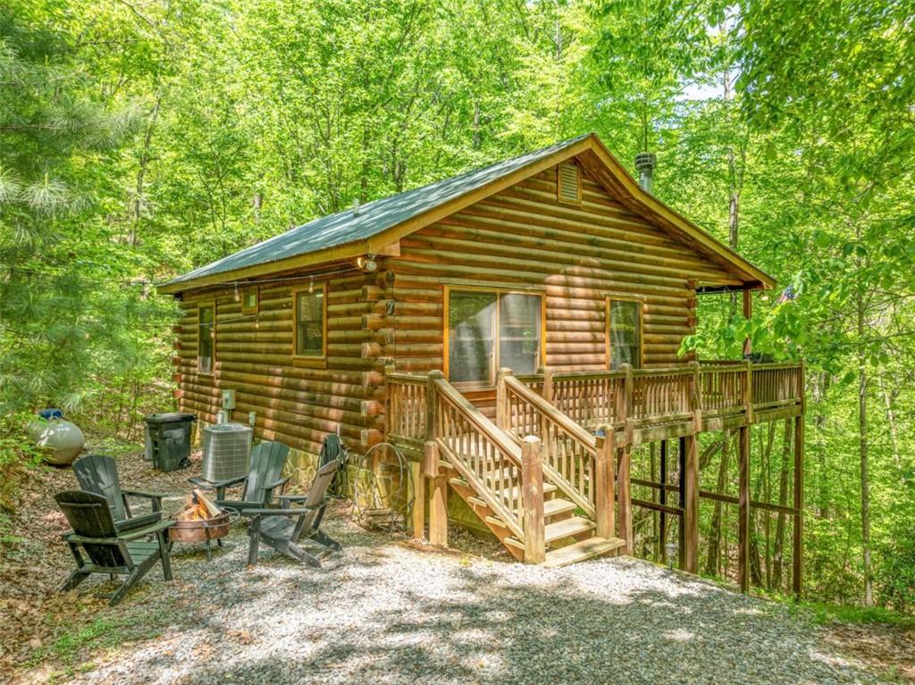 Freshly updated with new interior paint, stylish furnishings, and curated accessories, The Wildwood House is the perfect blend of rustic charm and stylish, modern comfort. Nestled on a serene 1.5+ acre corner lot in the scenic Cherry Lake subdivision, this true-log cabin invites you to unwind in style. Step inside to find a warm, inviting great room wrapped in rich tongue-and-groove wood finishes and anchored by a cozy, wood-burning fireplace - perfect for snuggling up on chilly mountain nights. The open-concept kitchen, featuring cheerful green cabinetry and modern appliances, flows seamlessly into a dining area with seating for four, making entertaining easy and relaxed. With 2 bedrooms, a full bath, and a laundry closet all on one level, the layout is smart and efficient-ideal for low-maintenance living or hosting guests comfortably. The bedrooms have been color drenched in soothing mountain tones to keep the rustic warmth yet still being modern. Step outside and embrace the mountain lifestyle on the expansive wrap-around porch. Soak your cares away in the private hot tub while listening to the sounds of nature or gather around the firepit under the stars with friends and family. Adirondack chairs, fireflies, and the peacefulness of the woods create the ultimate North Georgia experience. Located between the vibrant mountain towns of Blue Ridge and Ellijay, you're perfectly positioned for outdoor adventures like hiking and biking, visits to local wineries, or exploring boutique shops and farm-to-table dining. This turn-key cabin is ready for whatever you envision-whether it's a money-making investment, your weekend getaway, or a peaceful full-time home. Don't miss your chance to own this refreshed, rustic-meets-modern retreat. The Wildwood House is calling-come see it today!