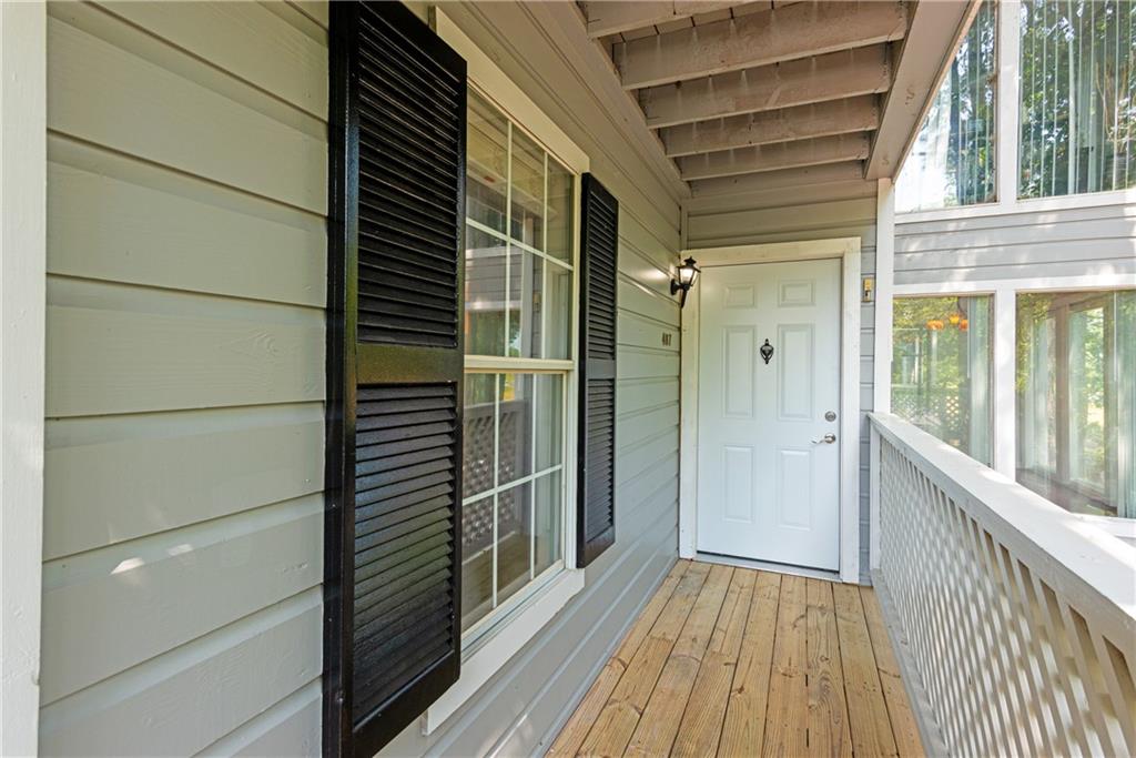 Exterior entry featuring light grey siding, black louvered shutters, a white entry door, and wood-finish flooring on the porch