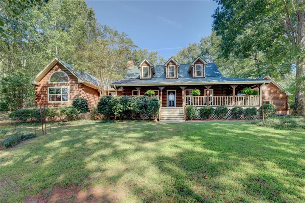 Welcome to your dream escape, a stunning Craftsman log house nestled on an expansive almost 7-acre oasis that perfectly marries rustic charm with modern luxury. This remarkable property offers an unparalleled lifestyle surrounded by nature, privacy, and endless recreational opportunities. Drive through the gated entrance, and you are greeted by a fully-fenced paddock on the right and a breathtaking view of the lake and manicured lawns on the left. Follow the driveway lined with fuchsia and white crepe myrtle trees, cross over the picturesque bridge, and up the hill to arrive at the main dwelling with a gorgeous trellis meeting you by the attached wood paneled garage. This captivating home is enveloped by lush woods, and is fully fenced in providing an unparalleled sense of privacy and tranquility. Step out front to your fully-stocked lake (shared with only one neighbor), ideal for leisurely afternoons. The boat dock beckons you to launch your mini electric pontoon boat which conveys with the house. The lake is the perfect backdrop for your tranquil lifestyle. Relax and unwind in your inground saltwater pool, complete with cascading waterfall. The back deck, with its built-in benches and dedicated dining alcove complete with a gas grill, makes for the perfect setting to host summer barbecues and peaceful evenings under the stars. Accommodate family and friends in style with a charming detached guest house featuring a variety of amenities. Horse lovers will delight in the two large stables. The heated/air-conditioned shop/garage/barn offers endless possibilities for hobbies, storage, or even a creative workspace. The main house boasts a master suite with spectacular lake views, a cozy sitting area, a warm fireplace, and a walk-in closet. An additional fireplace in the living room provides ambiance on cooler evenings. Step onto the wraparound porch, complete with a swing and brand new ceiling fans, where you can sip your morning coffee or enjoy sunsets. The property also features a raised garden house, allowing you to cultivate your green thumb, a chicken coop, and an RV port. Explore the natural bounty of wild blackberries, muscadines, chanterelle mushrooms, and walnut trees that dot the landscape. Don't miss your chance to own this piece of paradise-schedule a tour today and step into the life you've always envisioned. Easy 1 hour drive from Atlanta and 40 mins to Athens.