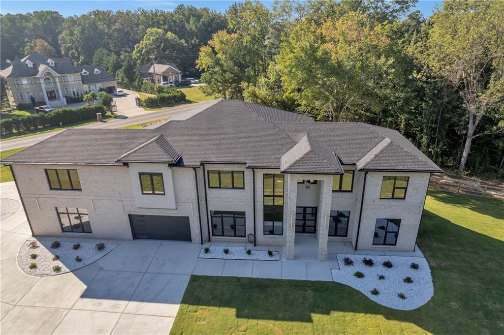 Step into this stunning gated estate, where modern luxury meets thoughtful design on a beautifully landscaped, fully fenced lot. The long circular driveway, sleek wrought-iron gate, and brick pillars create a memorable first impression, while aerial views reveal abundant space for outdoor living or a future pool.
Inside, wide-plank hardwood floors and oversized windows flood the open spaces with natural light. Two modern fireplaces with floor-to-ceiling designer finishes anchor the living areas. A dedicated first-floor home office offers a quiet, private workspace. The chef’s kitchen features a waterfall quartz island, premium cabinetry, professional appliances, and a walk-in pantry, complemented by a discreet secondary kitchenette/prep kitchen for effortless entertaining.
The serene primary suite offers a boutique-style walk-in closet and a spa-like bath with dual vanities, a makeup station, freestanding soaking tub, and a massive dual-rainfall shower with elegant gold fixtures. Secondary bedrooms each include walk-in closets and stylish en-suite baths. Additional highlights include a mudroom with built-ins, a large laundry room, ample storage, and a three-car garage with glass-panel doors and epoxy floors.
Outdoors, a covered patio with two ceiling fans and a built-in summer kitchen—grill, sink, and refrigerator—overlooks the expansive fenced yard, perfect for gatherings or pets. Combining privacy, craftsmanship, a convenient first-floor office, and proximity to shopping, dining, and major routes, this move-in-ready home balances elegance with comfort for the discerning buyer.