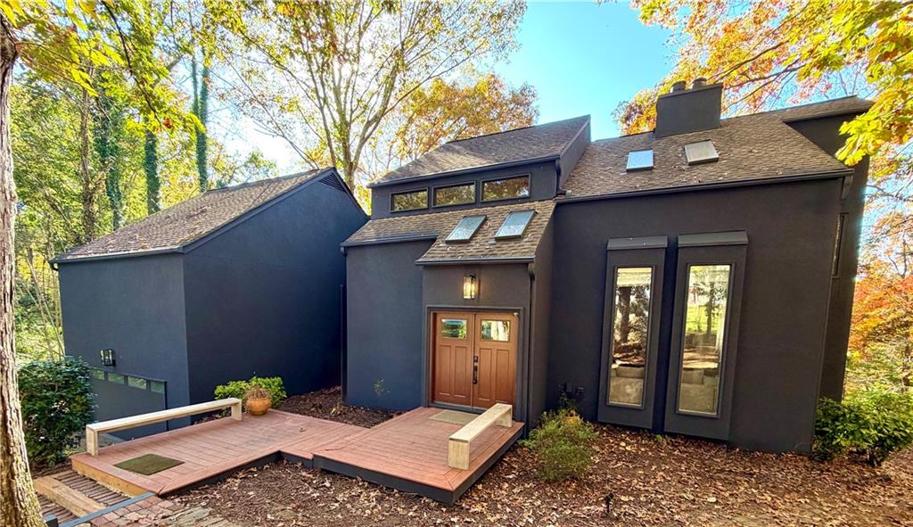 Back of property with a deck, a chimney, roof with shingles, and stucco siding