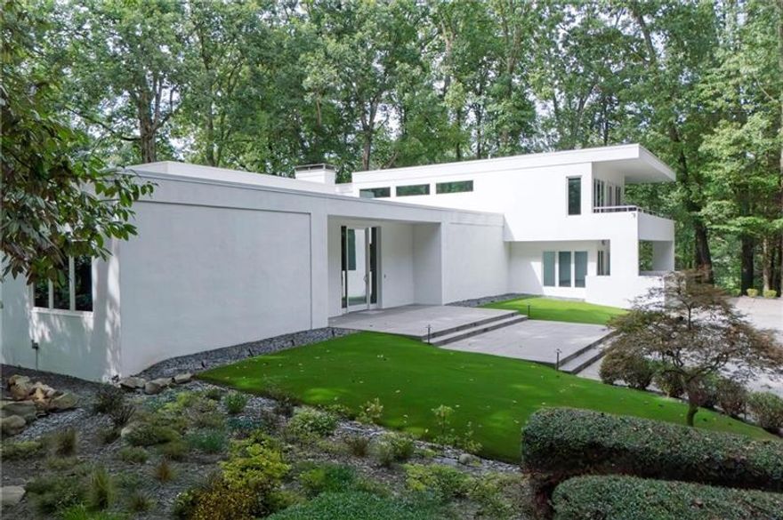 This spectacular contemporary estate on 2.5  private acres stands as a true landmark in Buckhead's prestigious Paces neighborhood. Sophisticated in design yet warm and livable, the property offers a rare balance of modern architecture and everyday comfort. A private drive leads to an expansive motor court, mature landscaping, and a turfed front lawn, setting the stage for the home's striking entrance. Inside, a dramatic foyer with 12-foot ceilings introduces sun-drenched interiors framed by walls of windows, soaring ceilings, and sleek contemporary details. The main-level primary suite boasts a newly renovated bath and an oversized custom closet. Designed for both everyday living and grand entertaining, the main level showcases a vast living room that also functions as a formal dining space for 12+, anchored by a large wet bar ideal for gatherings. Additional highlights include a private office, stylish powder room, and a comfortable family room. The chef's kitchen features stone counters, SieMatic cabinetry, Gaggenau ovens, an 8-burner Russell gas range, and a wine refrigerator, and flows seamlessly into a fireside breakfast room overlooking the lush, private backyard-complete with ample space for a future pool. Upstairs, two bedrooms and two bathrooms are complemented by a spacious bonus room that opens to a covered deck, perfect for year-round outdoor enjoyment. A possible fourth bedroom, currently serving as an office, enhances the home's flexibility. New windows throughout fill the interiors with natural light and frame views of the surrounding greenery. Outdoor living is equally impressive, with porches on both levels, expansive lawns, and multiple areas designed for recreation, relaxation, and entertaining. Located in the sought-after Jackson Elementary district and close to Buckhead's premier dining, shopping, and schools, this remarkable estate offers an unparalleled lifestyle in one of Atlanta's most coveted neighborhoods.