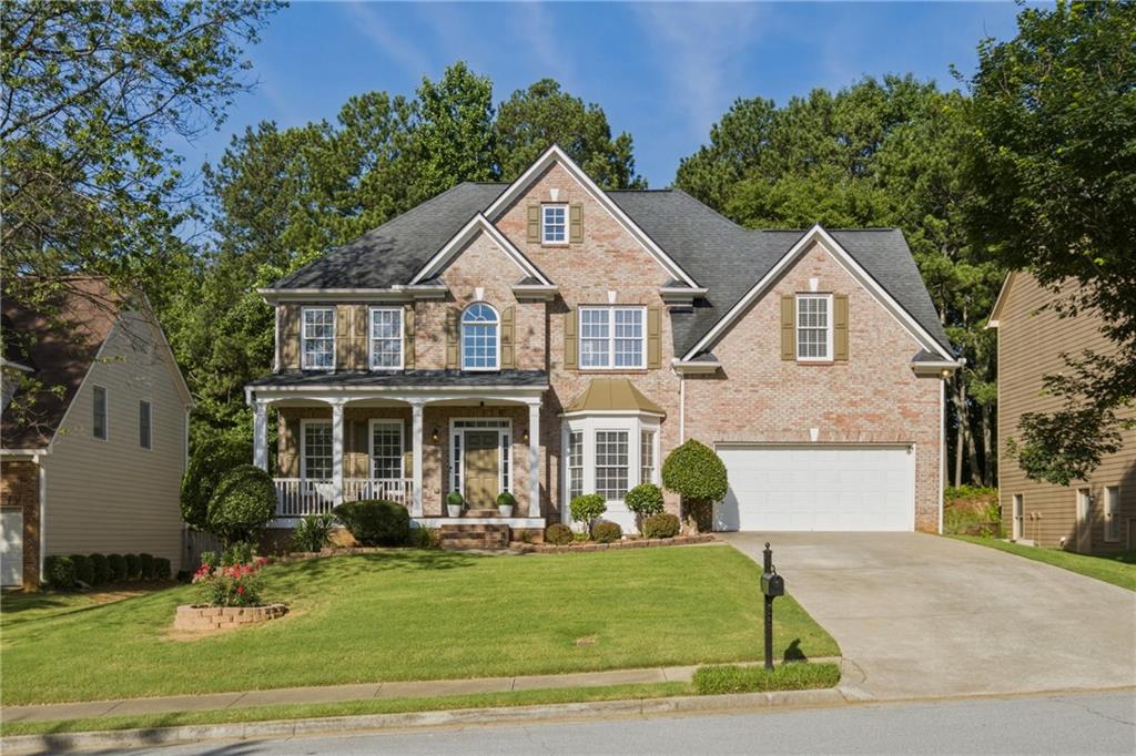Brick facade residence featuring a covered front porch with white columns, a two-car garage, multiple gabled rooflines, and a bay window