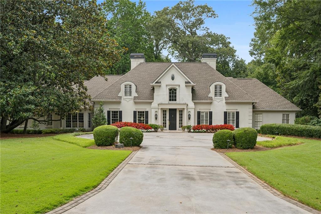 Nestled on 1.5 beautifully landscaped acres in coveted Kingswood, this exceptional residence blends timeless elegance with inviting warmth. Ideally located just moments from top private schools, major highways, and the Buckhead business district, the home offers a rare combination of convenience and seclusion. Tucked away in a serene, private setting, the property features lush, manicured grounds designed by Marcia Weber of Gardens to Love and a beautiful heated pool. Inside, the main level impresses with a light-filled vaulted great room and a bar that seamlessly connects to the grand two-story foyer, expansive living and dining rooms, and a generously sized kitchen—perfectly suited for both refined entertaining and relaxed family living. The luxurious primary suite is also on the main level, complete with a spa-like bath renovated in 2015 with heated floors, and a custom-designed closet. A versatile guest suite and a handsome library/office and another bar, complete the main floor. The sunlit terrace level offers flexibility with a second office, abundant storage, and a fully equipped in-law suite with a full kitchen. Additional amenities include a whole-house generator, upgraded pool equipment, an irrigation system, and a transferable Aquaguard warranty and a S.I.R. stucco bond—adding comfort, peace of mind, and enduring value to this exquisite home.