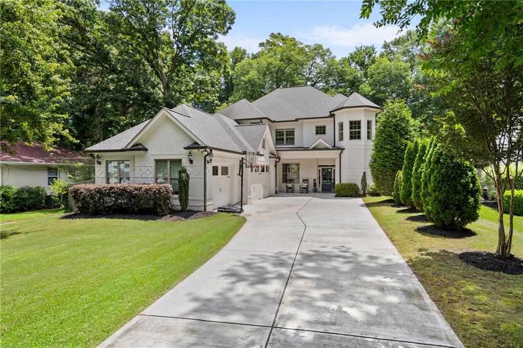 Tucked into one of Brookhaven’s most desirable pockets of Ashford Park, this stunning residence sits on a deep, tree lined lot offering privacy and a peaceful residential feel while being just minutes from premier shopping, dining, and parks. A timeless white painted brick exterior wraps three sides of this home, paired with a charming turret-style accent and inviting front porch. The long driveway leads to a 3 car garage and sets the home elegantly back from the street, boosting curb appeal and functionality. Step inside to a bright, spacious foyer that opens to a dramatic dining space beneath an intricate coffered ceiling. Rich hardwood floors and wide-open sight lines lead into an open concept living room filled with natural light, built-in shelving, and seamless access to the backyard. The kitchen impresses with sleek white cabinetry with marble counters, a large island with seating, a high end wolf appliance package, and a walk in pantry designed for both everyday living and entertaining. Just off the kitchen, a tucked away office nook offers a perfect remote work zone. Also on the main level, a private guest suite with a full ensuite bath is ideal for visitors or in-laws, complemented by an additional half bath for convenience. Upstairs, a versatile loft landing serves as a playroom, reading area, or media zone for kids or guests. The spacious primary suite is a true retreat, complete with a private balcony overlooking the fenced backyard and a luxurious ensuite bath featuring dual vanities, a soaking tub, a separate shower, and a generous walk-in closet. Three large secondary bedrooms and a full upstairs laundry room add everyday convenience and comfort. Out back, enjoy a flat, fenced in yard perfect for kids, pets, or future plans to add a pool. Multiple outdoor living spaces including a covered porch make relaxing or entertaining a breeze. Located just moments from Town Brookhaven, vibrant dining along Dresden Drive, upscale shopping in Buckhead, and the convenience of MARTA, this home blends suburban serenity with unbeatable access to the best of city living.