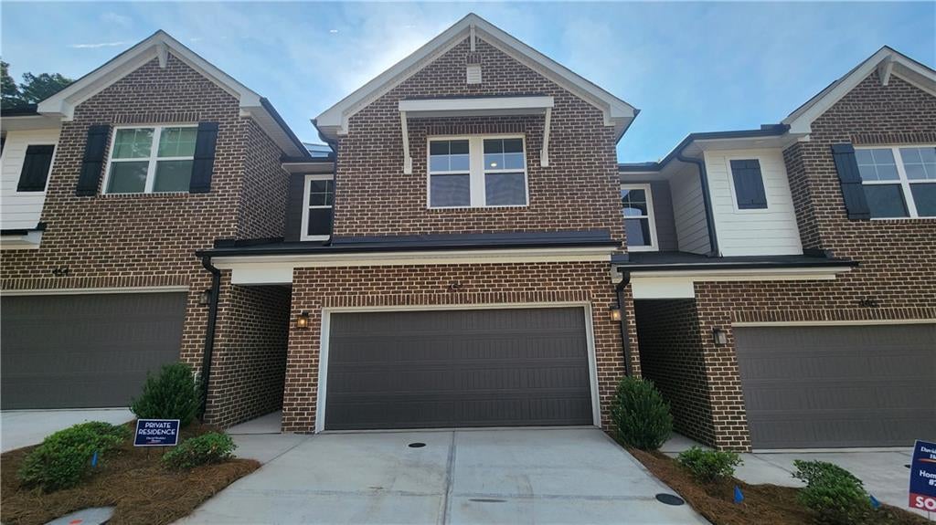 Brick townhome exterior featuring an attached garage with a dark gray door, a front entry awning, and dark window shutters