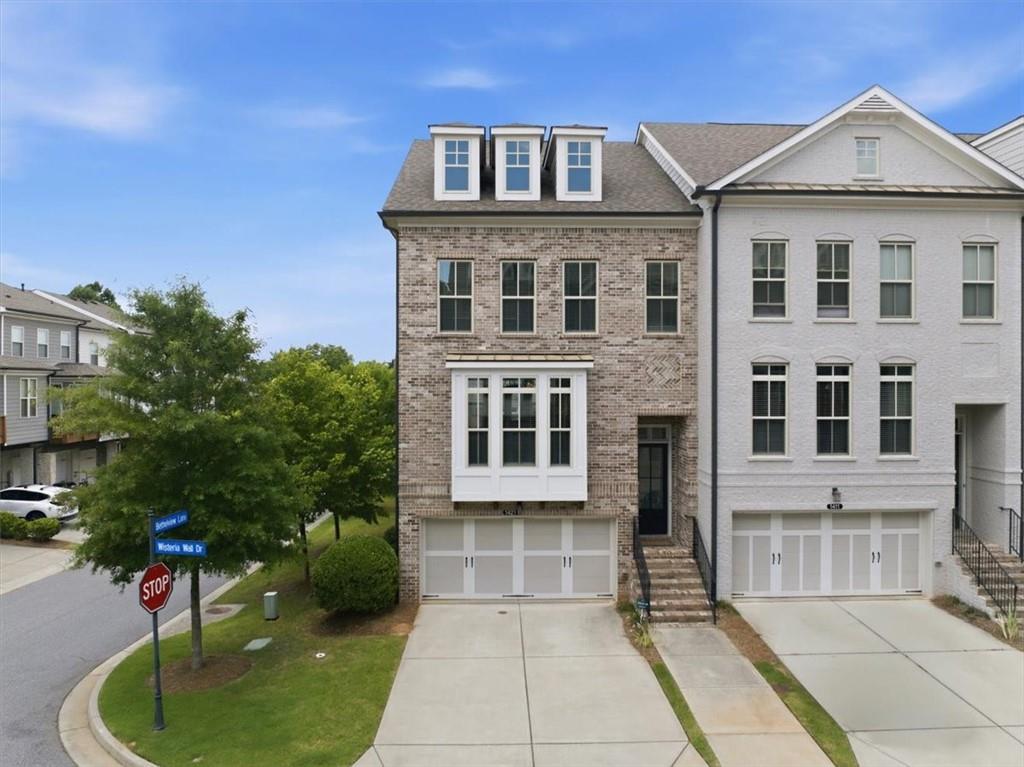 Brick facade townhome featuring a bay window, dormer windows, and an integrated two-car garage