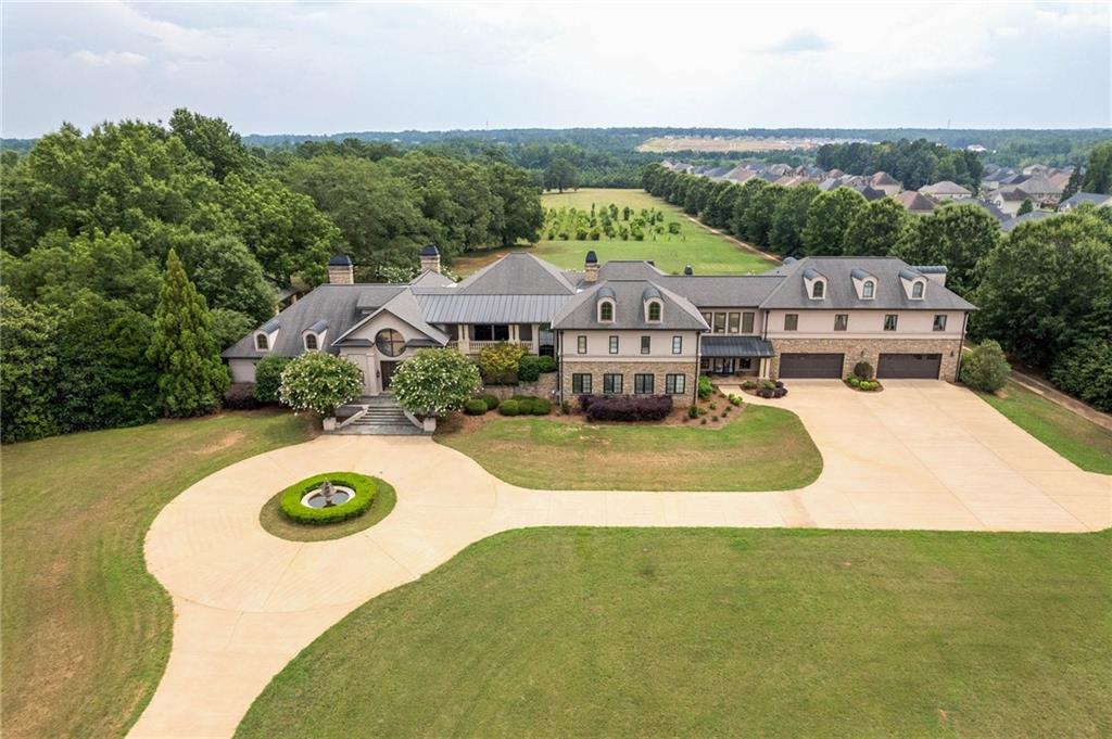 Welcome home to the exclusive DEERFIELD ESTATE. From the gated entrance and grounds of this Magnificent 12,200 sq. ft. European Style Masterpiece to the unparalleled elegance, luxury and grandeur of the interior, you will be enchanted! Property was fully renovated in 2000. Spanning 3 levels, this home offers 7 stunning bedroom suites and 8 bathrooms, and is situated on 50 acres of level land creating a park-like setting with 2 lakes and a private Vineyard. Sheer opulence awaits just beyond the front entrance. As you enter the main level, you are greeted by the Grand 2-story foyer with sweeping spiral staircase, soaring ceilings with both stained glass & vertical windows that drench the home in natural light, above the glistening tile and inlaid hardwood floors of the echoing corridor. Marble columns frame a sunken Grand gathering room with fireplace and built ins which flow into the elegant, banquet size dining room and in to the gourmet kitchen with breakfast room and keeping room with coffered ceiling and stacked stone fireplace. Main level also boasts multiple butler’s pantries, a separate staff kitchen and laundry as well as a concession area to service the Home Theatre and offers access to the 4 car garage and incredible outdoor entertainment spaces. The exquisite primary suite is also on main level with tray ceiling, double sided fireplace and an ensuite with tile, luxurious soaking tub, separate dressing room, multiple vanities and walk in closets, and a morning room with coffee bar and fireplace with access to pool and entertainment space out back. The 2nd level offers an open study space and piano nook, a recreation/gym or billiard room and a guest or Au Pair Bedroom Suite with bath and kitchen. There is also an elevator that services each floor. 2nd floor further boasts 4 more Bedrooms each with their own spacious ensuite and access to an exterior covered 2 story veranda. Rounding out the interior of this incredible home, is the 3rd floor which features the vaulted 6th bedroom and full bath. *Exterior grounds of home features incredible outdoor entertainment space with resort style lap pool flanked by a pool house on one side and outdoor kitchen, bar and grill pavilion on the other. Not to mention, home is nestled on 50 lush, level acres of land with 2 pristine Lakes and a bountiful, working Vineyard. Property is perfect for hosting large scale grand events with family and friends as well as enjoying small, intimate outdoor relaxation set to the backdrop symphony of birds, butterflies and wildlife. *Property would also make a perfect Wedding Venue, Bed & Breakfast or Golf course. Conveniently located only 20 mins from Atlanta Airport.