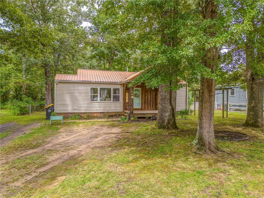 This cozy ranch-style retreat is nestled on a wooded lot just minutes from the shopping and dining conveniences of West Rome. A welcoming front porch sets the tone for this charming home, inviting you into a warm interior filled with natural light and rich wood flooring. The kitchen offers generous cabinet space and flows seamlessly into the main living area, creating a comfortable space for everyday living and entertaining.
Bedrooms are thoughtfully positioned for privacy and comfort, offering a peaceful place to unwind. Step outside to enjoy a spacious fenced backyard surrounded by mature trees, ideal for relaxation or outdoor gatherings. A patio provides the perfect spot for morning coffee, while the outbuilding offers extra storage or space for hobbies. With its blend of character, functionality, and proximity to local amenities, this property is a true hidden gem.