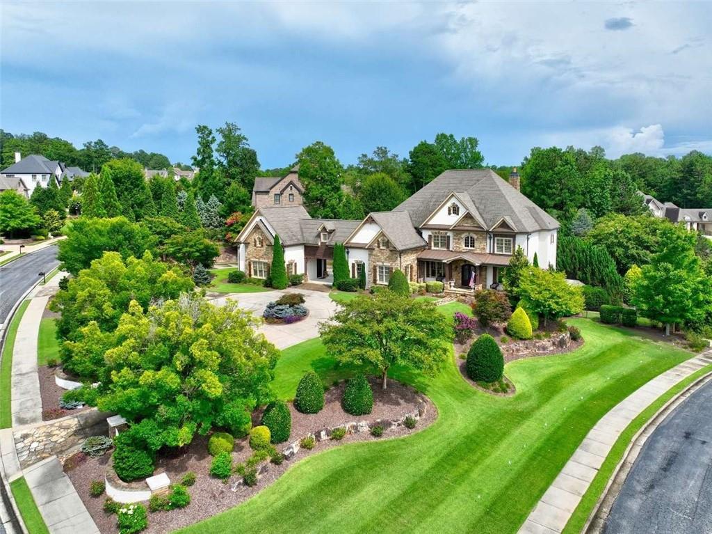 Welcome to Luxury Living in the Heart of Milton! Located in the prestigious, guard-gated Manor Golf & Country Club, this custom-built estate offers over ~9,000 sq ft of heated/cooled living space on a beautifully terraced 1.19-acre corner lot with views of the Tom Watson Championship Golf Course. This 6-bed, 7 full bath & 2 1/2 bath home is designed for entertaining and comfort, featuring 10-ft ceilings, custom crown molding, floating staircase, and abundant natural light throughout. The expansive main level includes a gourmet kitchen with Wolf & Sub-Zero appliances, oversized island, double sinks, pot filler, warming drawer, and dual Asko dishwashers. Enjoy an adjacent walk-in pantry with rolling ladder, command center desk, and mudroom with 2nd laundry. The open floor plan flows into a stunning keeping room with vaulted ceiling, Palladian window, and stone fireplace. A formal dining room and wet bar with wine cooler make entertaining easy. The guest suite on main includes a large ensuite bath and tray ceiling. Step outside to a resort-style backyard with covered patio, outdoor kitchen (Viking grill, side burner, fridge), wood-burning fireplace, pool with hot tub & sun ledge, firepit, and lush seating areas. Professionally landscaped by Cartwright Landscapes, the backyard also features 350+ linear ft of custom stone walls. Upstairs, the primary suite features a triple tray ceiling, fireplace, spa bath with double showers, rain head, large bench, and a custom dressing room with 8' vanity. A breezeway leads to the private executive office suite above garage bays 4 & 5, with vaulted ceiling and private access for early departures or late returns. Three additional upstairs suites offer walk-in closets and private baths, plus a large bonus room with built-in desks, storage, and tech space. Main laundry is also upstairs. The finished terrace level includes a full kitchen with large island, full fridge/freezer, icemaker, microwave, range, and dishwasher. Enjoy a large den, game area, media room (10 seats, 86” Sony TV), gym with rubber flooring and steam shower, private bedroom with full bath, and workshop/craft area. Tech closet is fully wired for smart home integration, with network, audio, video, and coax pre-wired throughout. 5 garage bays, circular drive, and extended parking behind the portal garage make hosting easy. Community amenities include: 24-hour security, clubhouse, fitness center, restaurant, indoor/outdoor pools & tennis (hardcourt & clay), sidewalks, and world-class golf. Close to top-rated schools, Hwy 400, and shopping/dining in Milton, Alpharetta, Halcyon, and Avalon.
