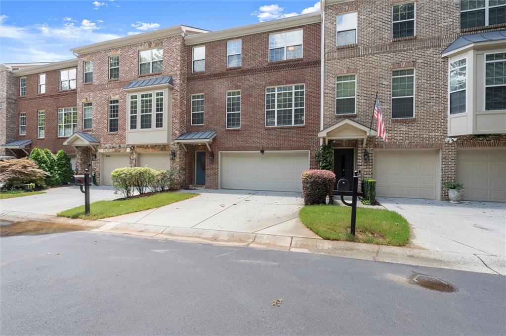 Multi-story townhome featuring a brick exterior with stone accents and a bay window
