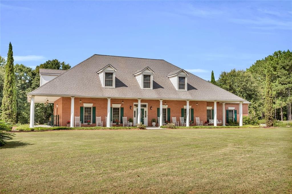 Southern Living at its finest This 4-bedroom four sided brick estate home is beautifully situated on 7.7 acres of highly desirable level land with hardwoods, peach trees, blueberry bushes, flowering gardens of crepe myrtle, gardenias, camellias, roses, and azaleas, with a separate fenced gardening area. The home invites you to get away to your oasis. It is set back on the property for the ultimate privacy and features 10 foot-wide covered rocking chair porch in an L design with 13 fiberglass columns for solid aesthetics and ease of maintenance. Enter into the home with rich solid hardwoods throughout and newly installed plush carpeting. A front living room is privately set apart for the perfect afternoon of reading. The large dining room can accommodate a large table for the holidays. The chef's kitchen has been updated with stone counters, custom white cabinetry, under-cabinet lighting, a gas cooktop, double ovens, and an undermount sink—the laundry room and powder bath complete this area. The home welcomes family gatherings in the den with its tiled surround fireplace and floor-to-ceiling style windows. The owner suite on the main level provides a large walk-in closet, a spacious area for reading or office and overlooks the private yard with entrances to the porches and full-length windows. The spa bath has a jacuzzi tub, a wide shower, and beautiful white tile. The upstairs has three oversized secondary bedrooms with large closets and additional storage options. The additional 30 by 40 workshop on the property offers double roll doors, electricity, an additional (third) full bath for the shop/home, and additional storage areas. There are five frost-free spigots located around the property. The home is outfitted for easy maintenance with a central vacuum system, vinyl soffits, and fiberglass columns. This property is located in Loganville, with easy access to retail, restaurants, and parks and the added benefit of Walton County taxes. This beautiful estate is available for showings beginning on June 24 by appointment. Cinematic Video of property online.