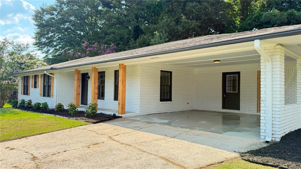 White brick exterior featuring a covered carport, dark framed windows with wood shutters, and wood-toned support beams