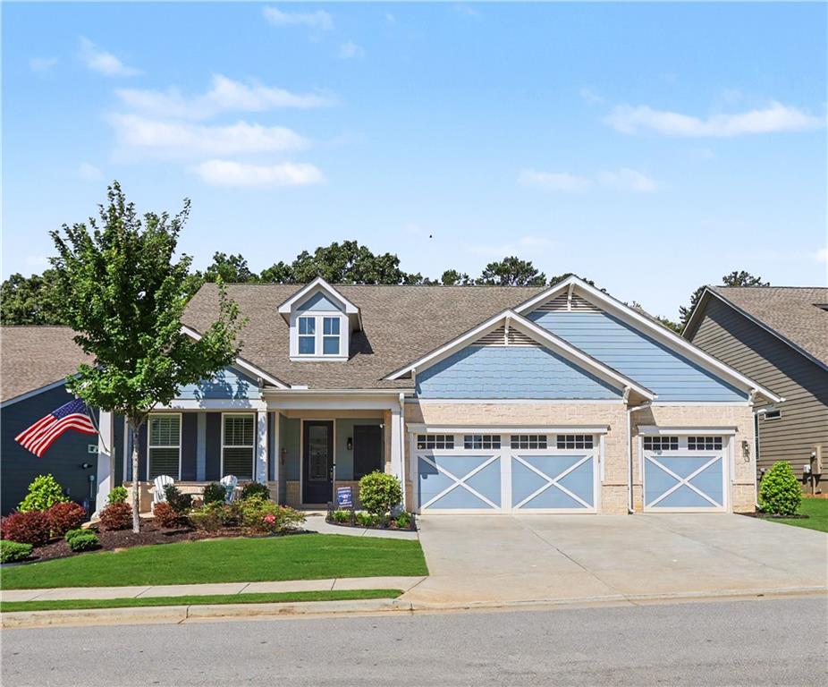 Blue siding exterior with a stone facade, featuring a covered front porch, dormer window, and an attached two-car garage with decorative doors