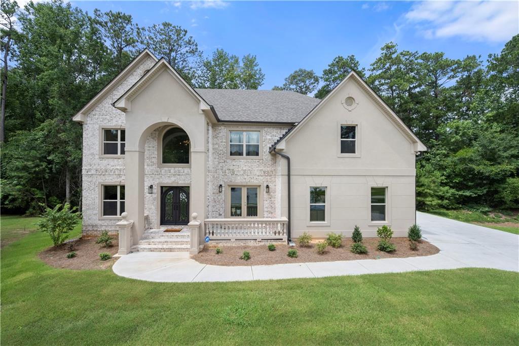 Welcome to this stunning, newly built four-sided brick home offering instant equity on a full basement perfectly situated on a quiet cul-de-sac with a three-car, side-facing garage offering both enhanced privacy and ample storage. With thoughtfully designed spaces and high-end finishes throughout, this home offers refined living in a peaceful setting just outside the hustle and bustle, while still being minutes from everything—including grocery stores, shopping, dining, coffee shops, top-rated schools, major highways, parks, and recreational facilities. From the moment you step through the double entry doors, you're greeted by a grand two-story foyer with hardwood floors that continue throughout the main level. The home exudes elegance with judges paneling in the formal dining room, decorative column accents, and a formal living room that can also serve as a stylish home office. The spacious, light-filled vaulted family room features coffered ceilings, a cozy gas fireplace, and views of the upstairs catwalk. The adjoining gourmet kitchen is as functional as it is beautiful, with granite countertops, a herringbone tile backsplash, stainless steel gourmet appliances, vent hood, walk-in pantry, and a large center island perfect for prep or casual dining. There's also an additional breakfast area that opens to the covered back deck, ideal for morning coffee or dining under the stars. A main-level bedroom and full bathroom make for a perfect guest suite or multi-generational living setup. Wrought iron spindles line the oak staircase that leads to the upper level, where you'll find the expansive primary suite with French door entry, double tray ceilings, and a separate sitting room. The luxurious en-suite bath features a huge walk-in shower with pebble stone flooring, freestanding soaking tub, dual vanities, and a massive walk-in closet. Upstairs also includes three secondary bedrooms, two full bathrooms, a conveniently located laundry room, and a flex space perfect for a reading nook, homework station, or creative zone. The unfinished basement is ready to be finished as it offers a blank canvas to design an extension of the home that not only adds equity but fits your lifestyle! Maybe a media room, home gym, game room with billiards table, bar area, or maybe you're looking to create in-law quarters or a young adult apartment. The opportunities are endless. With wooded backyard views, stunning interior details, and a prime location on the outskirts of Fairburn, this home offers the best of both luxury and convenience. A rare opportunity to own a new construction home with timeless character and room to grow!