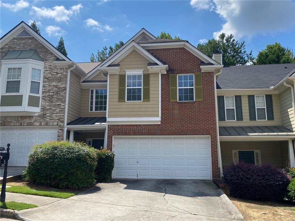 Multi-level townhouse exterior featuring a brick and siding facade, bay windows, two individual garages, and mature landscaping