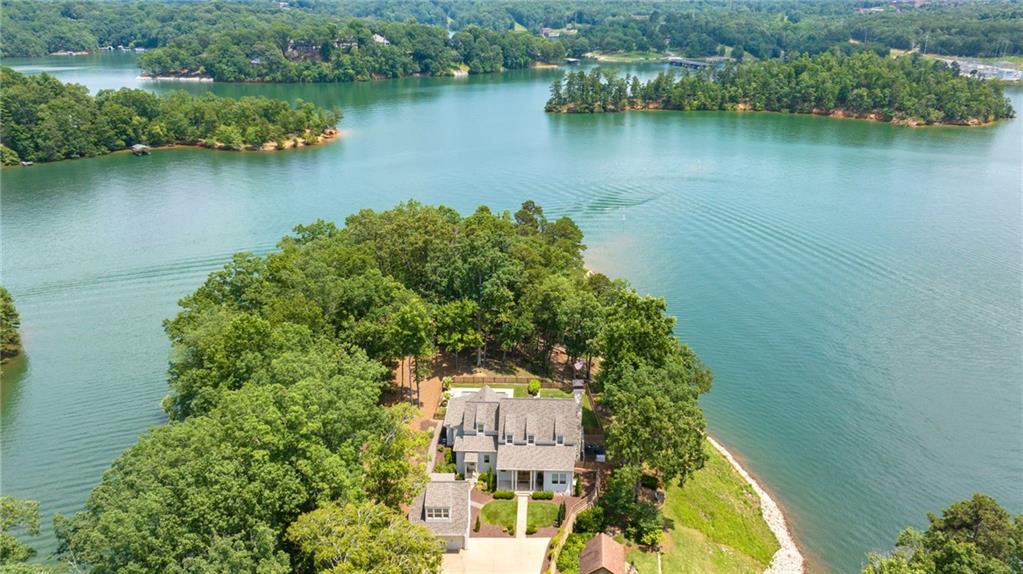 Southern coastal charm meets Lake Lanier luxury in this exceptional custom-designed estate, perfectly positioned on a private point lot surrounded by water and breathtaking lake views. Tucked away behind private gates and down a long, secluded driveway, this stunning home offers the ultimate in resort-style living, just minutes from the Chattahoochee Country Club and its private marina. Designed by renowned architect Stephen Fuller, this four-bedroom, four and a half bath residence blends timeless architecture with modern luxury. The home features a hardy shake and river rock exterior, beautifully landscaped shoreline with river rock detailing, and year round views from nearly every room. A heated pool, level fenced backyard, covered back porch, and two detached two-car garages complete the outdoor oasis. Inside, the open-concept layout is filled with natural light and framed by walls of glass, maximizing the lake views. The two-story foyer opens into a vaulted great room with a stone fireplace and an elegant dining space. The gourmet kitchen is a chef's dream, with quartzite countertops, a large island, custom cabinetry, stainless steel appliances including a six-burner gas range, and a spacious prep pantry that doubles as a bar and entertaining space. The main-level primary suite is a serene retreat with views of the pool and lake, and a spa-inspired bath featuring a soaking tub, dual vanities, custom shower, and two walk-in closets. A second main-level bedroom and full bath offer flexibility for guests or a home office. Upstairs, a central gathering area leads to two generous en-suite bedrooms with custom closets. Additional highlights include a welcoming office area off the kitchen, a large laundry room, and an unfinished daylight terrace level with approximately 2168 square feet ready to be customized. Modern conveniences abound, with a whole-house generator, natural gas for cooking, fireplaces, heating, and pool, plus an irrigation system, professional landscaping, and outdoor lighting. This home is a rare opportunity to enjoy the best of lakefront living, thoughtfully designed for both everyday comfort and exceptional entertaining.