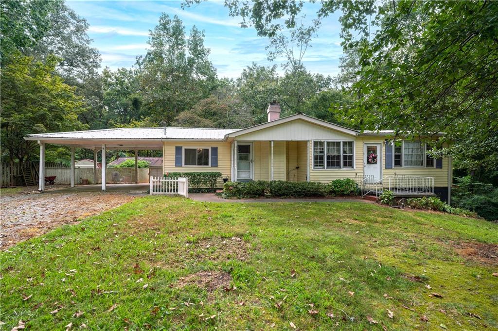 Welcome to this classic ranch-style home nestled on a beautifully wooded and private lot with no HOA and endless potential. Situated on nearly 2 acres, this property offers a serene escape with room to breathe, grow, and make it your own. Step onto the covered front porch, one of two separate entrances into the home, and enjoy the peace and quiet of your surroundings. Inside, you're greeted by a warm and inviting family room featuring rich wood flooring, abundant natural light, and a cozy fireplace—the perfect place to relax or entertain guests. Just off the family room, the kitchen boasts rustic white cabinetry, plenty of countertop and cabinet space, and a layout ideal for everyday cooking or hosting. A separate dining room offers space for formal meals or family gatherings, conveniently located near both the kitchen and living areas. The home's second entrance opens into a spacious great room—a flexible space that can serve as a secondary living area, home office, playroom, or entertainment zone. This room includes built-in bookcases, wood flooring, and is ready to be customized to fit your lifestyle. The primary bedroom is generously sized with natural light and wood flooring, while two additional bedrooms offer comfortable space for guests or family. A shared full bathroom features a vanity with added storage and a shower/tub combo. Downstairs, a partial basement provides even more possibilities. This area includes a partially finished secondary full bath and could easily be transformed into an additional living area, home gym, or bonus room. With walk-out access to the backyard and a separate side entrance, it’s perfect for multigenerational living or a potential rental opportunity. Outside, enjoy the expansive backyard surrounded by trees for total privacy. The back deck features both a covered section—ideal for all-weather relaxation—and an open-air portion, perfect for grilling and soaking in the sun. A detached workshop on the property provides additional storage or could be converted into a fantastic game-day hangout or creative space. Additional highlights include: Covered 2-car carport with extra driveway parking, No HOA, complete privacy, a spacious yard to plant a garden and enjoy nature. This home offers a great investment opportunity with room for updates and personalization! Whether you're looking for your forever home or an investment with potential, this property offers the best of country living with flexible spaces and a layout that can grow with you. While offering lots of privacy, this home is centrally located within minutes of local shopping and restaurants, as well as all of the amazing local amenities that Downtown Canton has to offer such as The Mill, Etowah Park, and so much more.