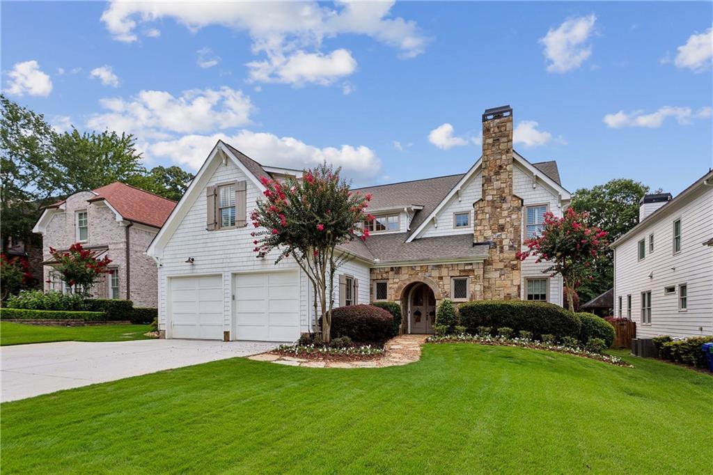 Located in Ashford Park on a fabulous street, this beautifully updated custom home boasts an incredible outdoor living area with a stunning pool. Great curb appeal begins with white shingle siding, a stone-arched entry, and elegant curved double front doors. Inside, the inviting foyer leads to a handsome office with a wall of built-ins, rich judges paneling, and a fireplace with a marble surround. The hardwood floors continue into the dining room and fireside living room, where a beamed ceiling, built-ins flanking a stacked-stone fireplace, and abundant windows frame views of the covered patio, pool, and backyard. A dry bar adjacent to the living room is ideal for entertaining. The living room flows seamlessly into the chef’s kitchen, which continues the beamed ceiling detail. This space includes a large island with seating, custom cabinetry, an appliance garage, a gas cooktop, stainless steel appliances, and a walk-in pantry. Nearby are a spacious laundry room, a mudroom/drop zone, a half bathroom, and access to the two-car garage. The main-level primary suite impresses with a soaring wood-paneled ceiling, hardwood floors, plantation shutters, and a marble-detailed en suite bathroom. Features include dual vanities, a separate makeup vanity, a soaking bathtub, a marble shower, and a large custom closet that conveniently connects to the laundry room. Upstairs, a generous landing offers the perfect TV area and leads to four spacious bedrooms and two bathrooms, one with dual sinks. The outdoor living space is spectacular, with a covered patio off the main living area featuring a stacked-stone fireplace, a flagstone floor, and a dining area. A built-in grilling station nearby includes a gas grill and a Big Green Egg. The walkout patio flows directly to the refreshing pool, complete with tranquil waterfalls and a stone diving board. The fully fenced backyard also includes lush landscaping and a grassy play area. Located in the Ashford Park Elementary School district, this home offers easy access to the shops and restaurants on Dresden Drive, Brookhaven, Buckhead, I-85, and all the perks of city living.