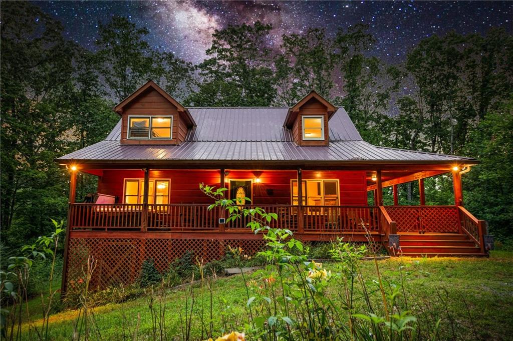 Escape to your own mountain retreat in the heart of Ellijay, an ideal opportunity for both personal enjoyment and investment potential. Nestled in the scenic North Georgia mountains, this charming cabin offers the perfect blend of rustic character and modern comfort. A spacious wrap-around porch welcomes you with panoramic views, while the open-concept interior features soaring vaulted ceilings, a cozy stone fireplace, and oversized windows that flood the home with natural light. The kitchen and living areas flow seamlessly, creating a warm, inviting space for gatherings. The private master suite includes an en-suite bath, and additional guest accommodations provide plenty of room for family or renters. Outside, a private deck overlooks the beautifully landscaped backyard—perfect for grilling, entertaining, or simply relaxing in nature’s embrace. Sold fully furnished and turn-key, this property is ready for immediate use as a vacation home or short-term rental. With its desirable location, strong vacation appeal, and versatile layout, it offers the perfect balance of mountain living and income-producing potential.