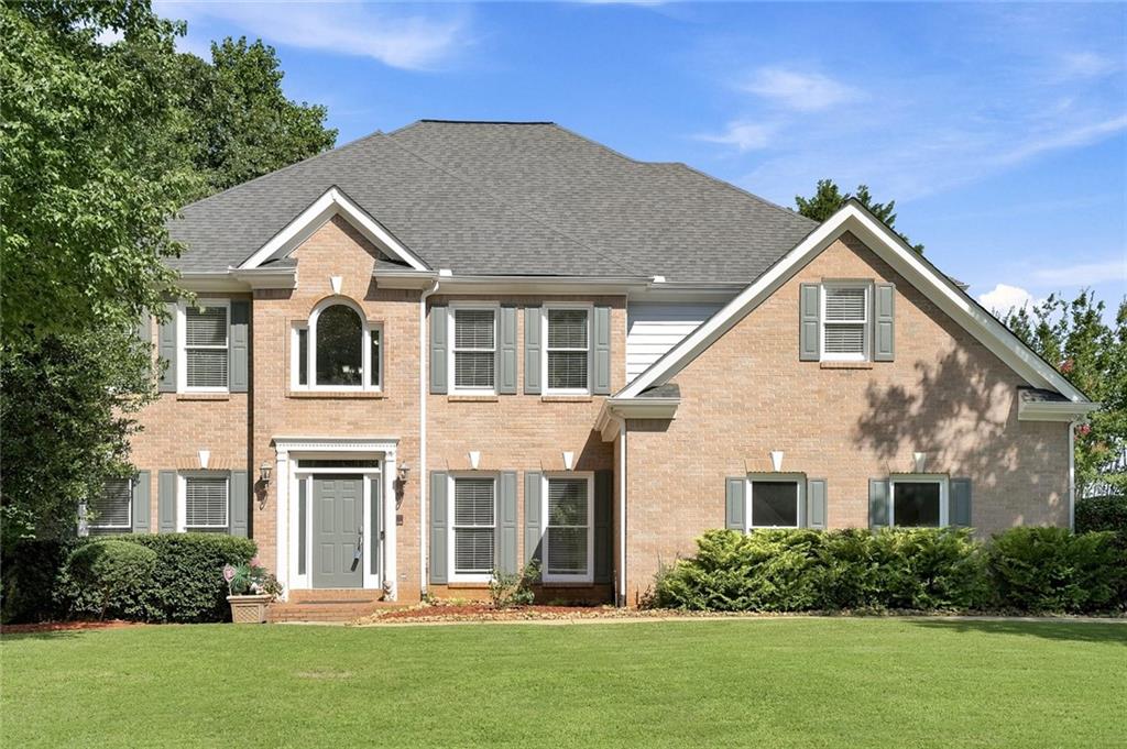 Brick fa?ade residence featuring a prominent gabled roofline, dark gray shutters, a central arched window, and a symmetrical front entry with a transom window