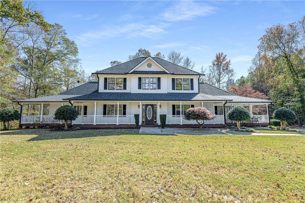Two-story residence featuring a white facade with dark shutters, a dark shingle roof, and a full wrap-around porch