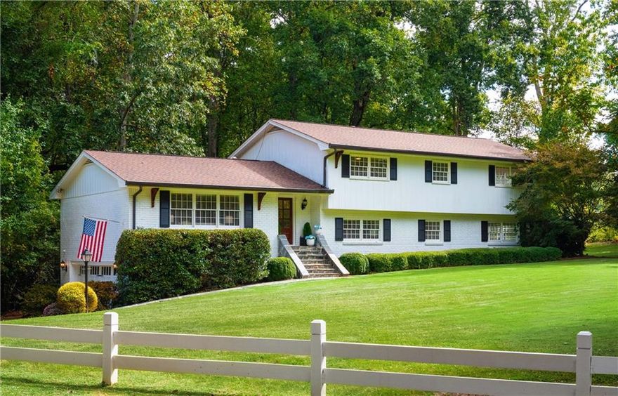 Timelessly reimagined for modern living, this Brookhaven residence rests gracefully on a sprawling corner lot encompassing two parcels, both of which convey with the sale. From the moment you arrive, the covered front entry and expansive front lawn create a distinguished sense of welcome, setting the stage for the beautifully renovated interiors within.

The main level unfolds with a formal living room off the inviting entry foyer, where three large windows frame views of the front lawn. A wide entryway provides division while seamlessly connecting the living room with the dining room, finished with wainscoting and two windows overlooking the backyard. At the heart of the home, the kitchen is a true showpiece, designed with white cabinets that rise to the ceiling, a bay window featuring a built-in eating area, an island, and professional-grade stainless steel appliances, including a double oven and a gas cooktop. Carrara marble tile forms the backsplash, complementing white quartz countertops and hardwood floors that continue seamlessly into the adjoining sunken family room. Here, a masonry fireplace and glass doors open to a covered patio with a striking stone fireplace, creating an effortless indoor-outdoor connection.
Upstairs, the oversized primary suite offers a serene retreat, featuring a spacious bedroom with a sitting area, dual walk-in closets, and a Carrara marble-detailed bathroom. This luxurious bathroom features a double vanity with a central makeup station, crystal chandeliers and a large seamless glass shower with floor-to-ceiling marble. Two additional bedrooms share an equally refined bathroom with double sinks, a makeup vanity, and a marble-clad bathtub/shower combination enclosed in seamless glass, along with dual product niches. A fourth bedroom is conveniently located on the lower level, served by a fully renovated bathroom.
Additional highlights include an updated laundry room with generous storage, a versatile recreation room with a wet bar, and a rare two-car drive-under garage. The expansive backyard provides an idyllic setting for both recreation and entertaining, featuring a Jacuzzi, a grilling area, a stone fireplace on the covered patio, and a wide, grassy lawn with ample space for a future pool.
Perfectly positioned between Brookhaven, Chamblee, Sandy Springs and Chastain, the home is moments from Silver Lake, Cambridge Square, Blackburn Park and Henri’s Bakery. With its rare Brittany Club core membership eligibility and potential for an income-producing suite with exterior access, this property combines lifestyle, location and luxury in one extraordinary offering.
