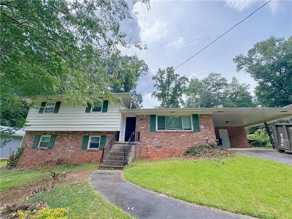 Split-level residence featuring a brick and white siding exterior, green window shutters, and a covered carport
