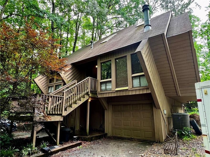 Calling all artists, visionaries, and lovers of the wonderfully unexpected—welcome to 2965 Pond View Ct, a truly unique contemporary diamond (literally!) in East Cobb. This is no cookie-cutter house. Designed and built by Tom Mozen—a local builder known for his bold, architectural creativity and his motto of never building the same home twice—this was the very first neighborhood he developed in East Cobb. And he made sure to start with a statement.

From the moment you arrive, you’ll notice the daring angles and striking shape of this diamond-shaped split-level home, tucked at the end of a quiet cul-de-sac on a private, wooded lot. Step inside and you’re greeted with an architectural centerpiece: a spiral staircase suspended by cables, leading to a private primary suite perched above the rest of the home. This suite includes a full bathroom and opens to a covered deck overlooking the backyard—an ideal retreat to sip coffee, read, or create.

On the main level, you’ll find two additional bedrooms and a full bath, with plenty of natural light and potential to update or reimagine. The unfinished lower level offers room to expand, with the potential for another bedroom, bath, studio, or media space. There’s also a two-car garage, and the shared driveway adds a touch of old-school charm to this hidden enclave. Ideally located in the heart of East Cobb, this home is just a short walk to top-rated Pope High School and zoned for some of Cobb County’s highest-performing public schools, with convenient access to shopping, dining, parks, and major highways like I-75 and GA-400—making everyday errands and commutes a breeze.

This home is being sold AS IS and is perfect for someone with vision, creativity, and an appreciation for bold design. It’s not just a house—it’s a conversation starter. If you’ve been searching for a fixer-upper with personality and serious architectural chops, this is the one.
