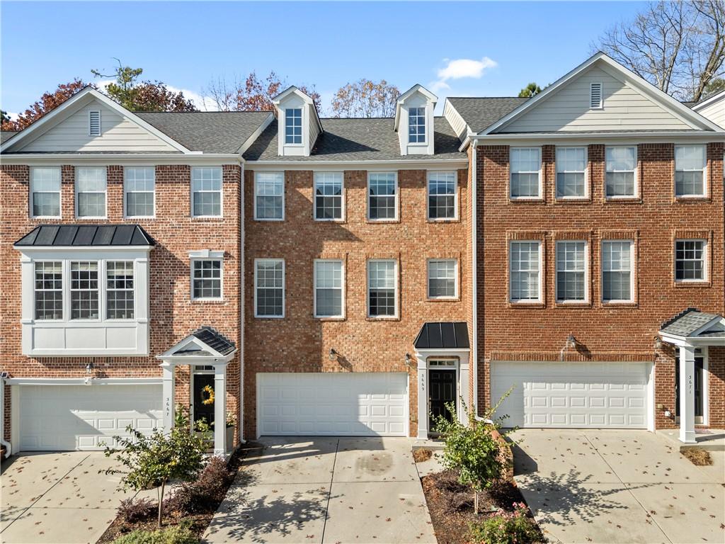 Colonial house with driveway, brick siding, and an attached garage