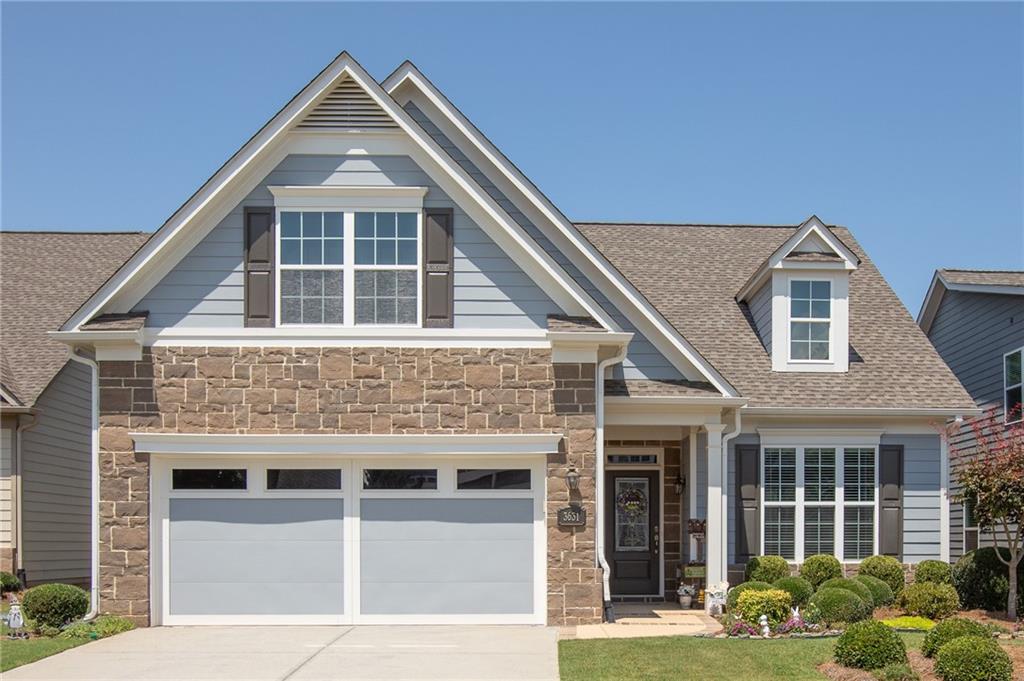 Two-story residential exterior featuring stone and siding finishes, a two-car garage with transom windows, a front entry with a dark paneled door, and a dormer window