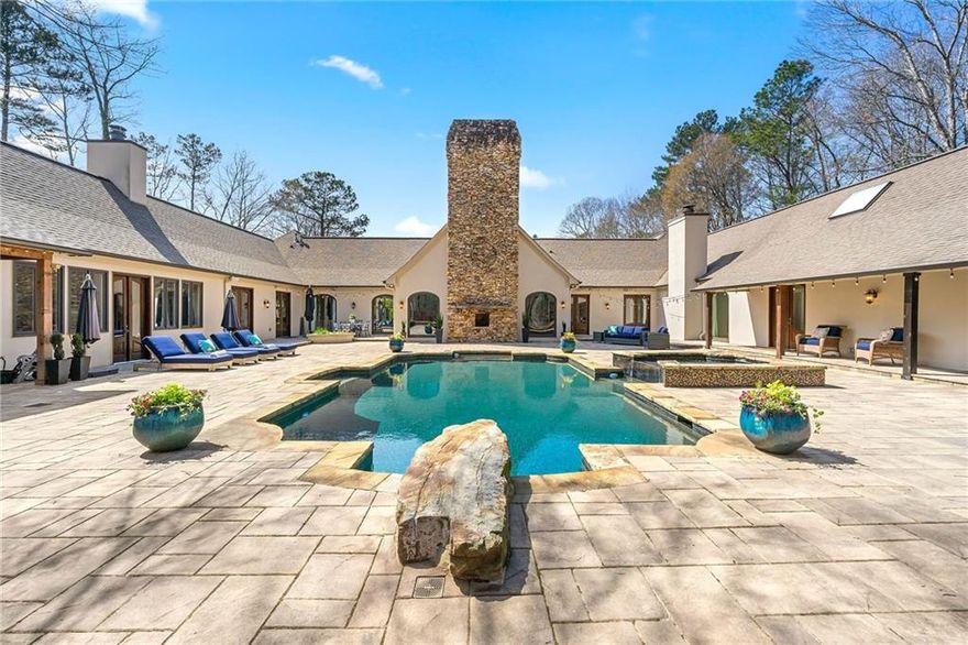Gated sanctuary wrapped within 4.5+/- acres in Buckhead! Wind your way through a tranquil, wooded property to an elevated and secluded house. Embodiment of one floor designed living, the house orients each oversized and light-filled living space with direct access and views to centralized outdoor space featuring: 4500 sqft patio, outside kitchen with pizza oven, pool, pool house, hot tub and gazebo. Enter the central wing through grand porte-cochere into a dramatic foyer and breathtaking living room with peaked 26 ft tongue/groove ceiling and majestic stone fireplace. Entertainer’s dream wing features a completely renovated kitchen with custom oak cabinetry, Calcutta Gold quartz island and matching countertops, two dishwashers, Wolf range, Subzero refrigerator and two full size wine refrigerators. This wing extends through the keeping room, with fireplace, into the peaked sunroom. Accordion doors then link the outdoor kitchen and external living room space to the entertainment wing. Expansive primary suite wing of the house includes private access to secluded outdoor retreat with fire feature. Renovated primary bath with dual vanities, separate tub and shower and large walk-in closet. Every bedroom boasts renovated ensuite bathrooms with pool house available as an optional nanny suite with separate entrance and full kitchen. The house uniquely combines indoor/outdoor living with the essence of the unparalleled property. Move in ready with over a million dollars of renovations.