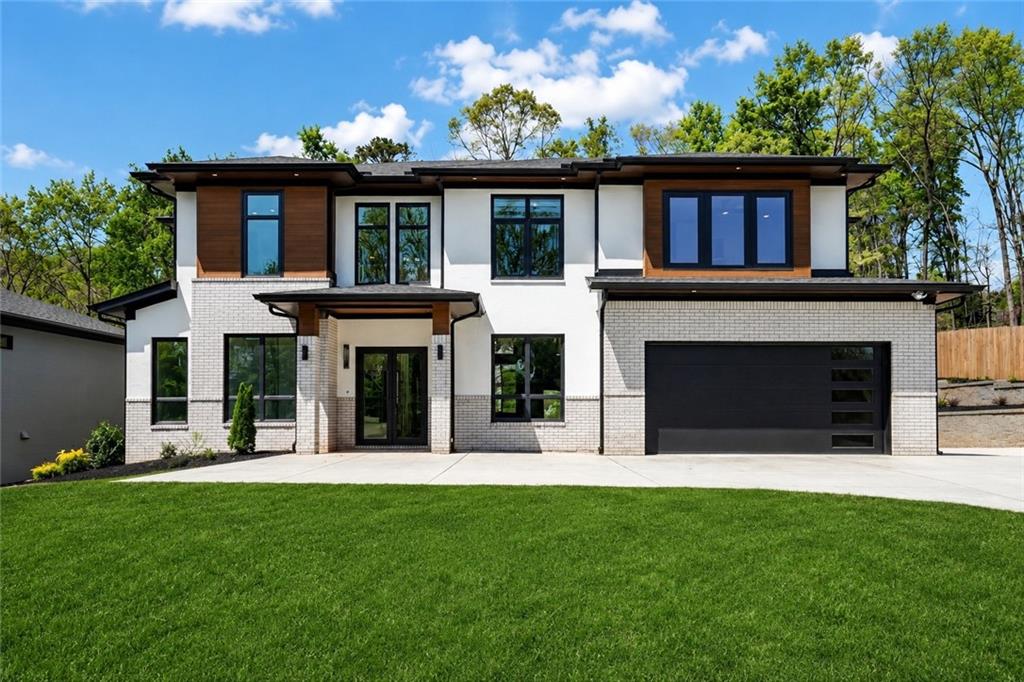 Contemporary residence featuring a white and light gray brick exterior with wood-finish accents, a black garage door with frosted panels, a concrete driveway, and a manicured front lawn