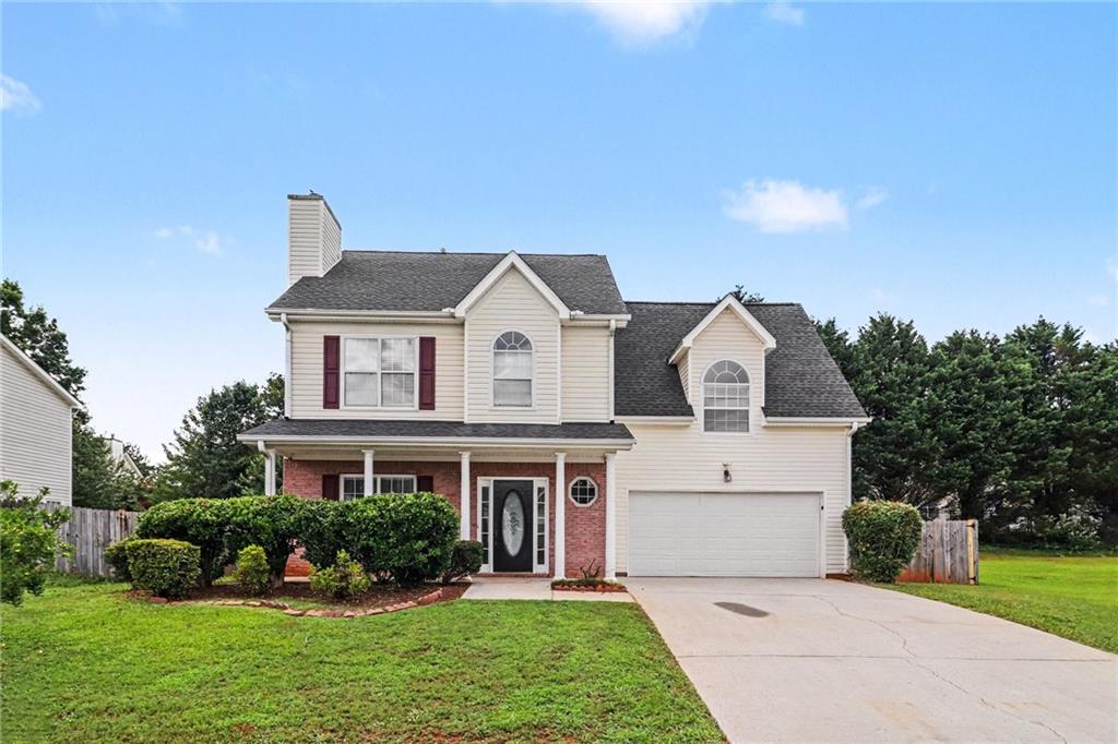 Two-story residence featuring a brick facade with white siding, a covered porch entry, an attached garage, a paved driveway, and mature landscaping