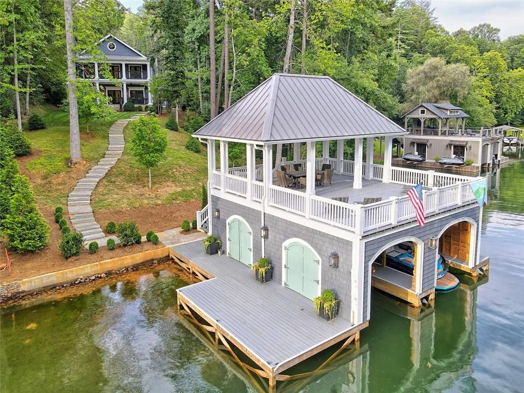 Everything to desire, lake-living-wise, is in this NEWLY constructed, custom-built home on Lake Burton. The Nantucket-cottage-styled home boasts four generous bedroom suites, with all marble baths, two levels of living areas, two outdoor decks, two expansive lofts and two half-baths. Beautifully appointed with designer finishes throughout including shiplap paneling, a classic white palette, rich hardwood floors and Restoration Hardware light fixtures and hardware. The main level features a generous master bedroom with a large walk-in closet, double sinks, elegant claw & foot soaking tub and a separate shower all outfitted in pristine white marble. Conveniently situated across the hall is the warm office/dining room and half bath. The stunning kitchen & great room is perfect for gathering with family & friends. The window-filled chef’s kitchen with hand-crafted painted cabinets and a huge center island is outfitted with a Thermador 6 burner gas range, Sub Zero custom paneled refrigerator, farmhouse sink, Kitchenaid dishwasher & Sharp drawer microwave. The middle level includes three ensuite bedrooms, a big laundry room, a large porch, a sitting area, and stairs to the upper level with two large lofts. The two levels of covered porches face the quiet cove and an architecturally matching, sunset-bathed boathouse with covered porch. The boathouse, which sports two electric lifts, is situated on deep, clear emerald green water and is a great area for safe swimming, kayaking & paddle boarding. This home is just waiting for a large family to bring their friends & start living the lake dream!!! It is the ONLY NEW build for sale on the lake and is only two minutes to Waterfall at Lake Burton and only 12 minutes to Clayton. The winding drive reveals plenty of private property and wonderful custom landscaping, and a two-car, detached garage complements overall aesthetics. Attention to every detail, such as an exterior in Hardie plank as well as solid-stone walkways to the boathouse, make this a lasting investment. Don't wait!! Call now to set up your appointment.