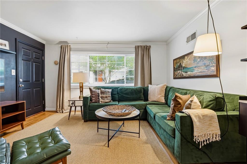 Living area featuring wood-finish flooring, a neutral tone carpet area, white crown molding, and a paneled entry door