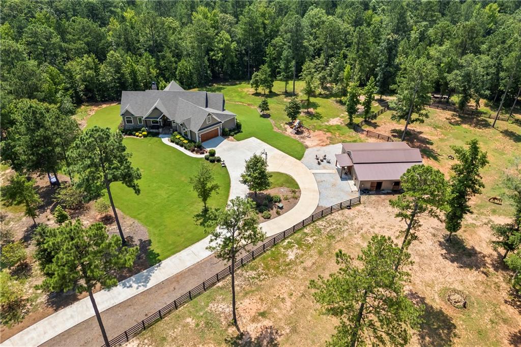 Welcome home to your own private sanctuary, nestled on ten peaceful, wooded acres with the perfect blend of modern luxury and timeless charm. Surrounded by mature pine trees and gentle rolling landscapes, this extraordinary five-bedroom, five-bathroom home offers quiet country living with close proximity to The Classic City, Historic Downtown Madison, and the luxurious shores of Lake Oconee. Step inside to an open-concept layout, where the heart of the home features a spacious living, dining, and kitchen area under 10 ft. vaulted ceilings with rustic wooden beams. The gourmet kitchen is designed for both beauty and functionality, with quartz countertops, a gas stove with pot filler, walk-in pantry hidden behind double doors, and a seamless flow to the large screened porch—ideal for entertaining or enjoying peaceful meals surrounded by nature. The owner’s suite on the main level is a calming retreat with large windows that invite in natural light and tranquil views. The spa-like bath features dual vanities, separate closets with built-ins, and a soaking tub. Two additional bedrooms on the main floor share a convenient Jack-and-Jill bath, offering privacy and comfort. Downstairs, the fully finished walk-out basement is perfect for extended living or hosting guests, complete with two en-suite bedrooms, a kitchenette, stone fireplace, wood-look tile floors, and a flex room ideal for a home theater, office, or dark bedroom. A dedicated gym space and abundant natural light make the lower level a favorite hangout spot. Upstairs, a spacious bonus room makes an ideal teen suite, playroom, or second office. Additional features include a large laundry room with prep area and sink, built-in storage from the garage entry, and a whole-home generator and a with a 500-gallon buried propane tank for peace of mind. The property continues to impress outdoors with a level lot, wide-open skies, and a three-stall horse barn built to match the home's aesthetic with plenty of storage for outdoor and equestrian equipment. Enjoy the ultimate in privacy and peace, whether you're sipping coffee on the screened porch or strolling your private acreage. As you venture from the home to the neighborhood amenities, you'll enjoy a private sitting area on the confluence of the Apalachee river and Hard Labor Creek. You'll also enjoy peaceful walking and riding trails through the common areas as well. From these common areas you can also kayak or canoe the waterways. Whether you're looking for a forever home or a peaceful escape, this one-of-a-kind property offers refined country living with unmatched serenity.