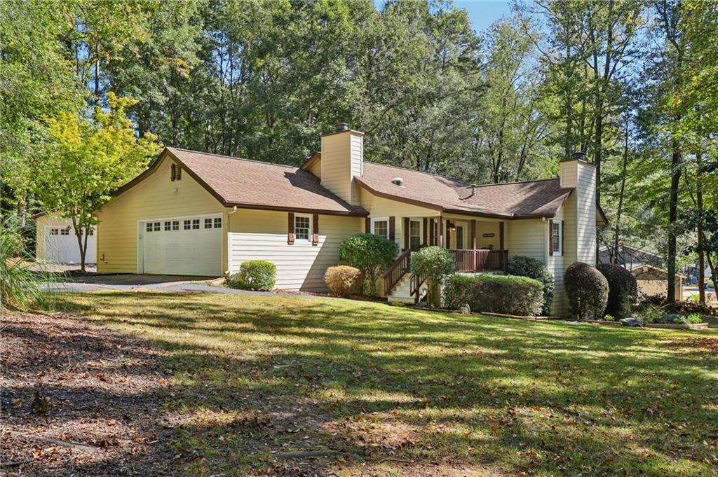 Ranch-style home featuring a chimney, a extra large golfcart garage, a front lawn, and view of scattered trees