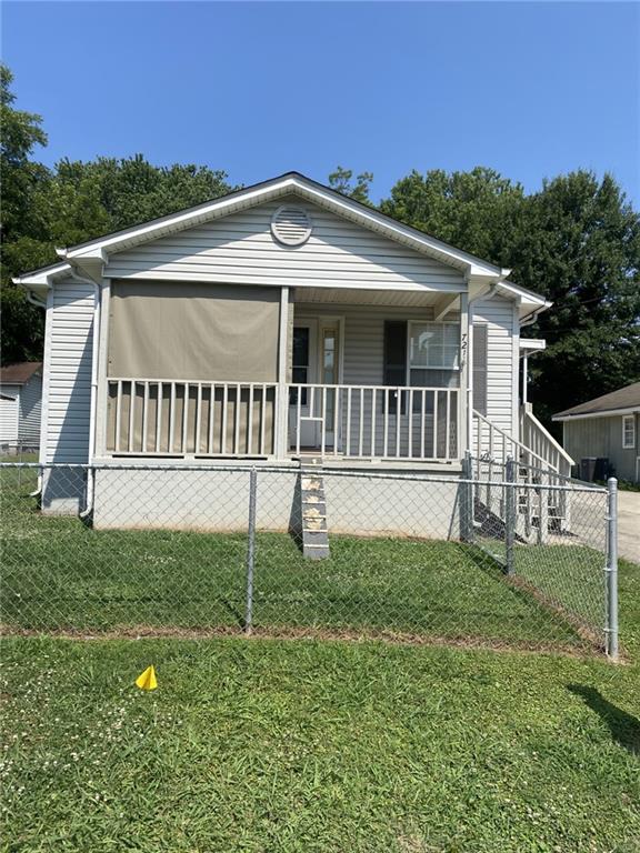 Front exterior featuring vinyl siding, a covered porch with a privacy screen, white railings, and a chain-link fence enclosing the front yard